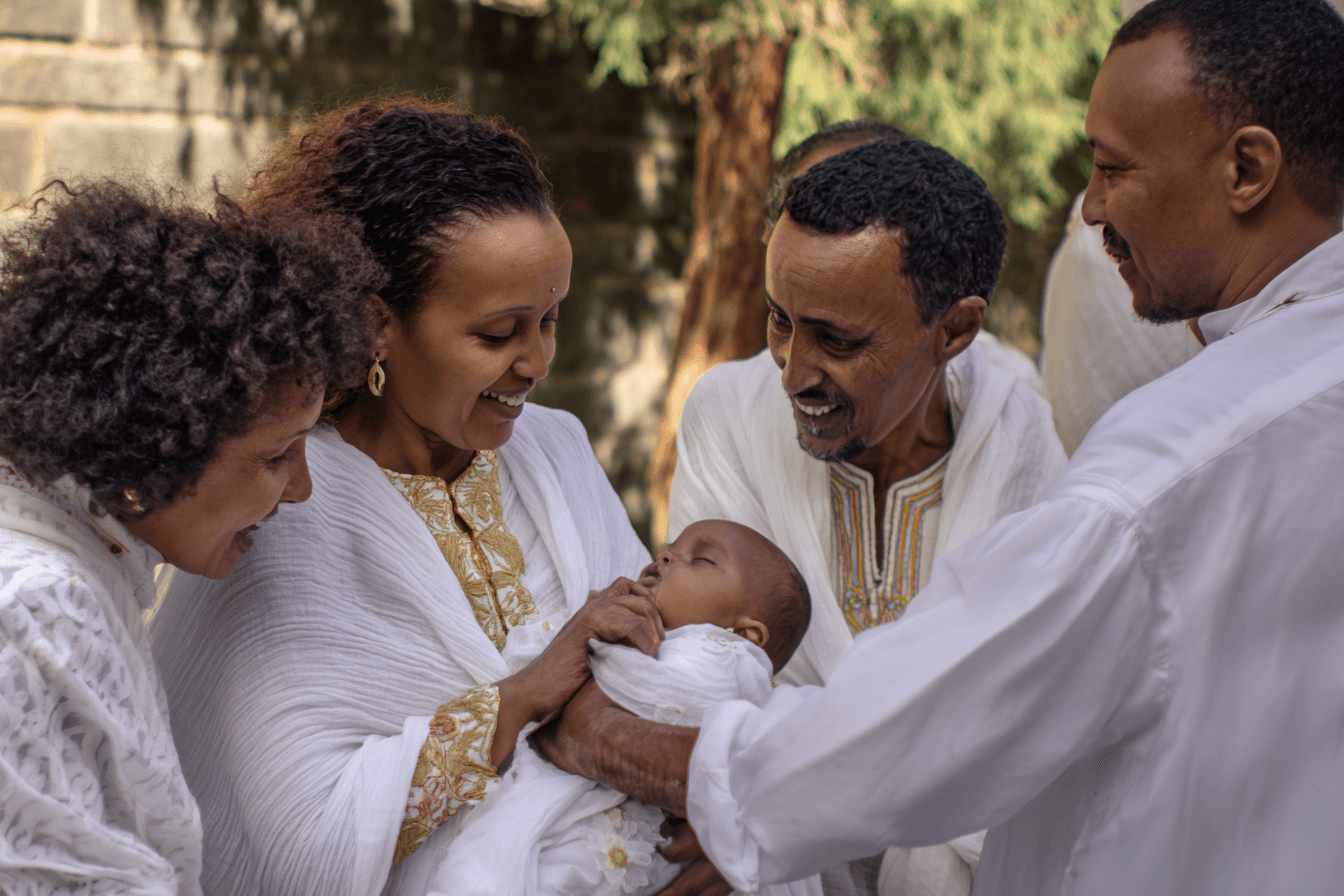 Ethiopian family gathered around newborn at christening ceremony all wearing white traditional dress